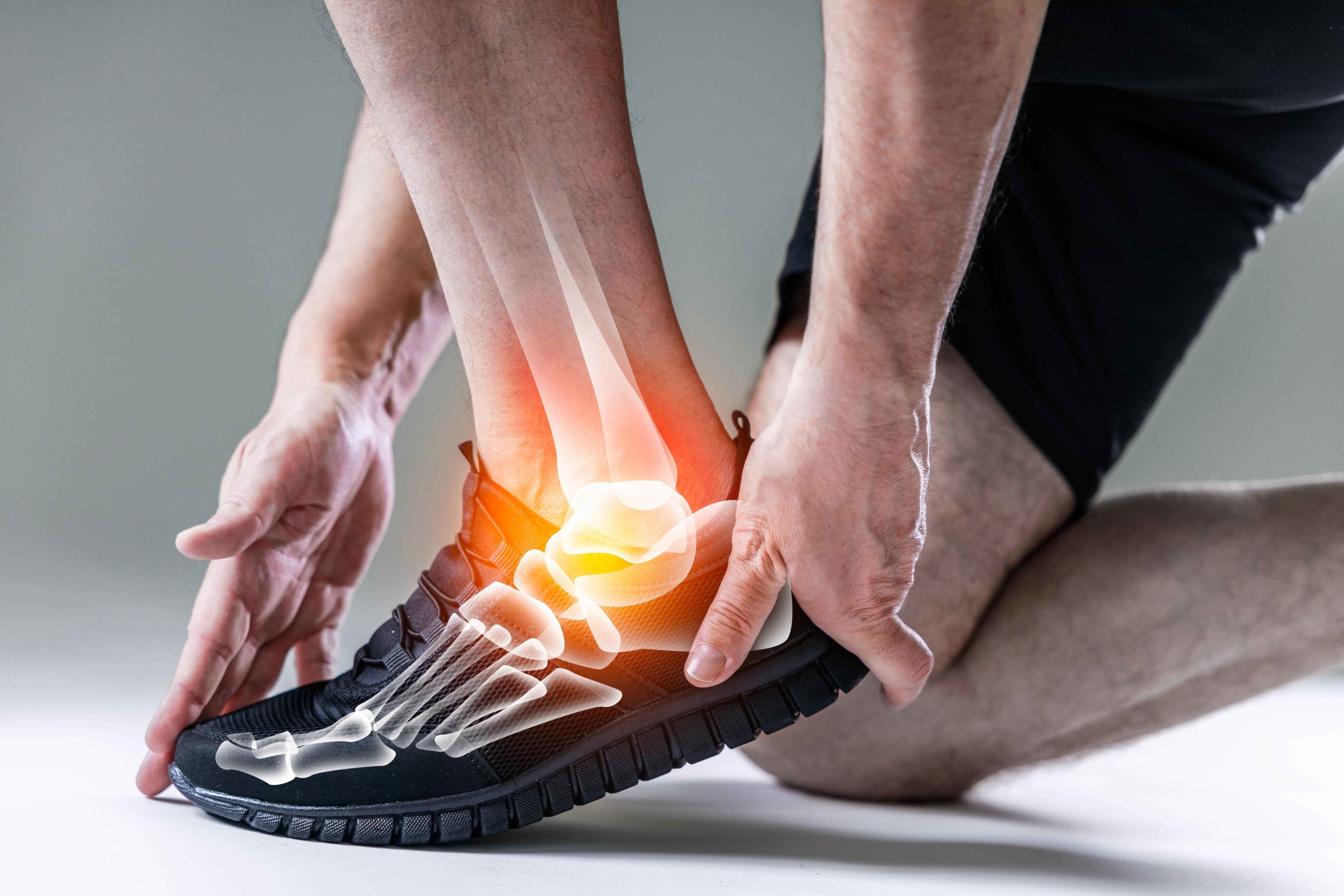 shutterstock_2464407867-min_11zon Mann kniet am Boden und hält sich den Fuß. Der Fuß ist anatomisch durchleuchtet und zeigt die Knochen und rot gekennzeichnet den Schmerzpunkt einer Verstauchung