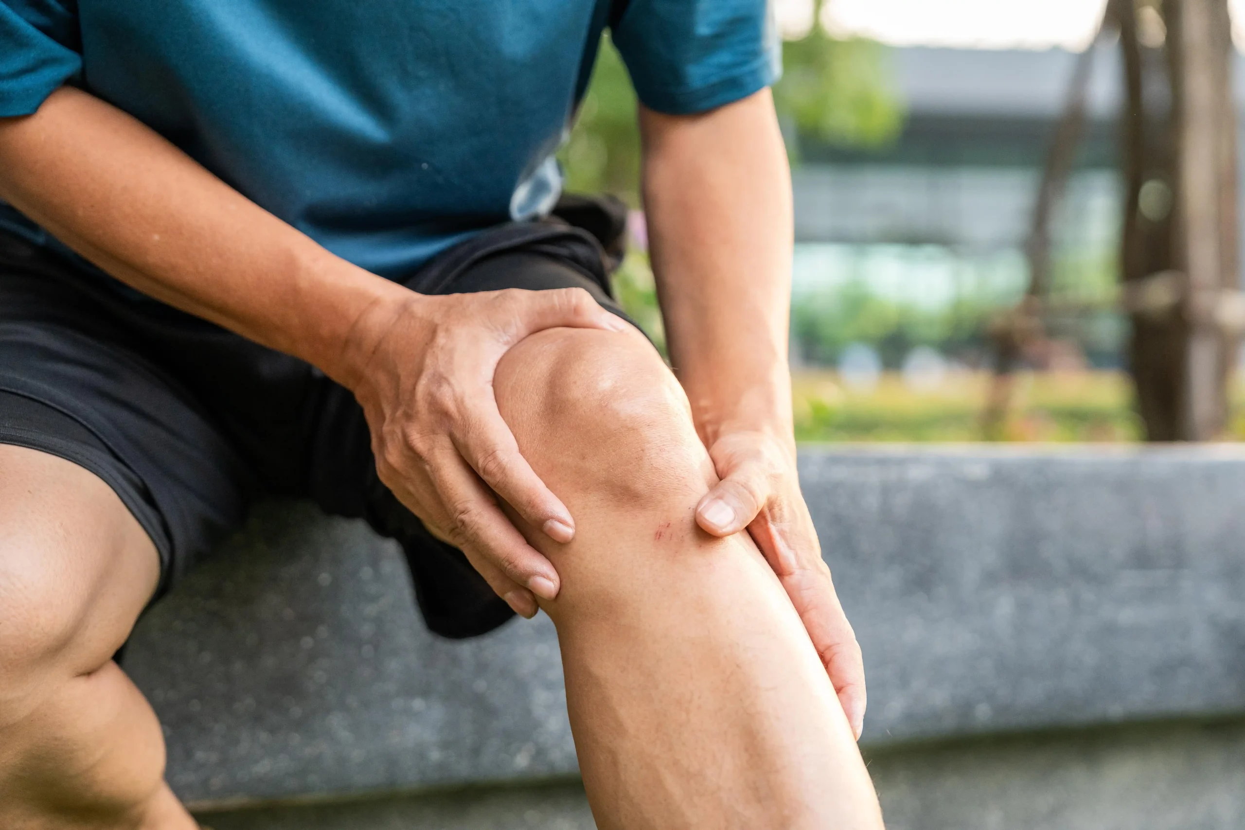 shutterstock_2468278869-min_11zon Mann sitzt auf einem Stein und hält sich sein Knie.